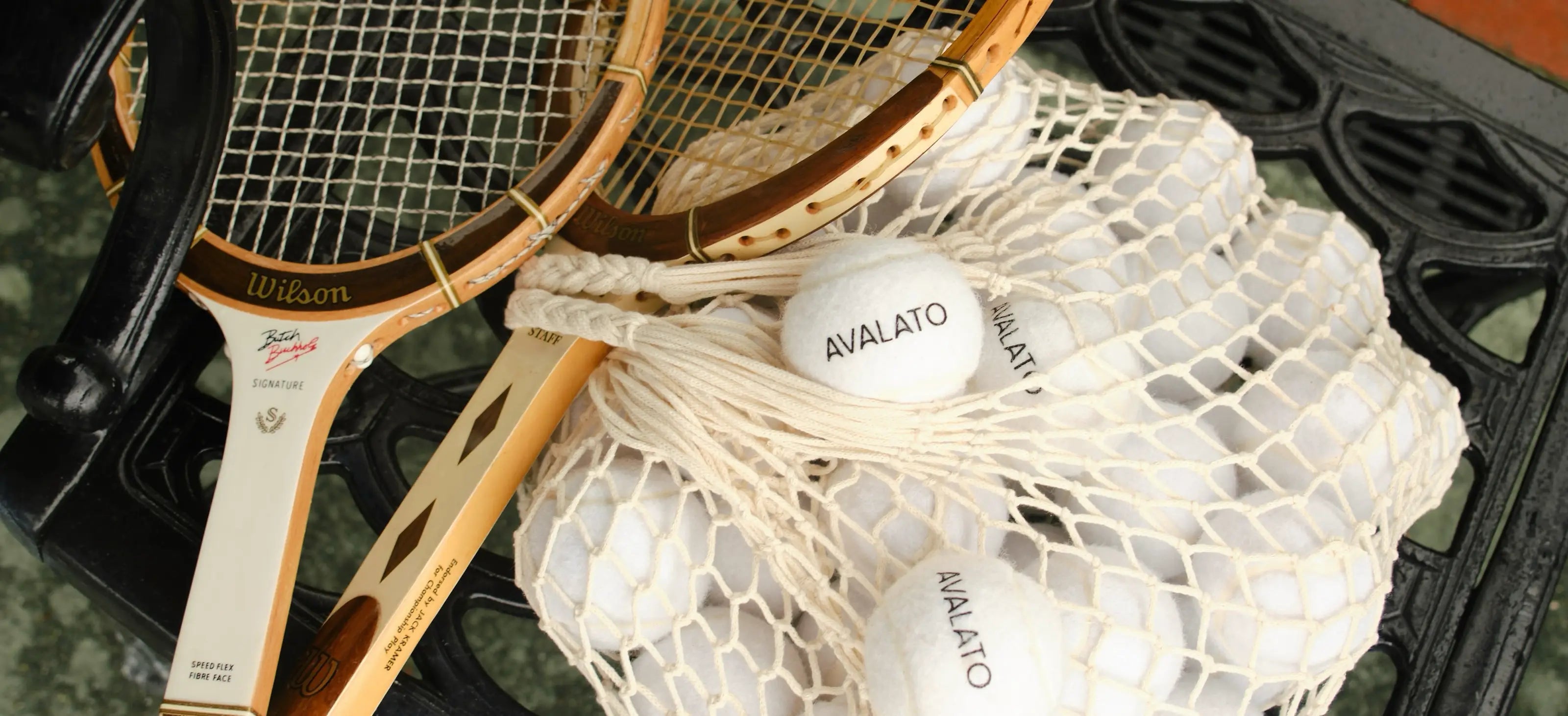 AVALATO white tennis balls in a net bag alongside wooden rackets showcasing vintage-style tennis gear