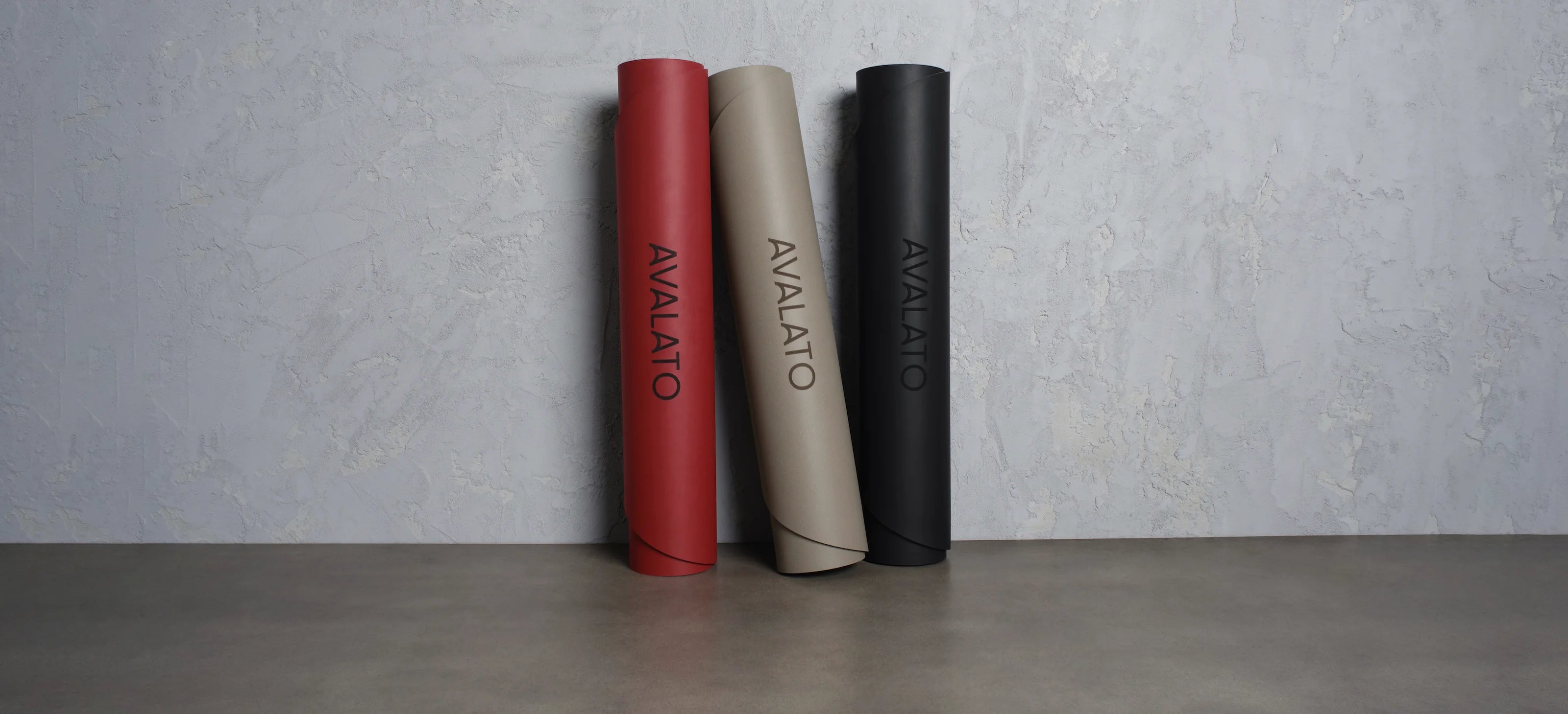 AVALATO exercise mats in red, beige, and black displayed against a textured wall