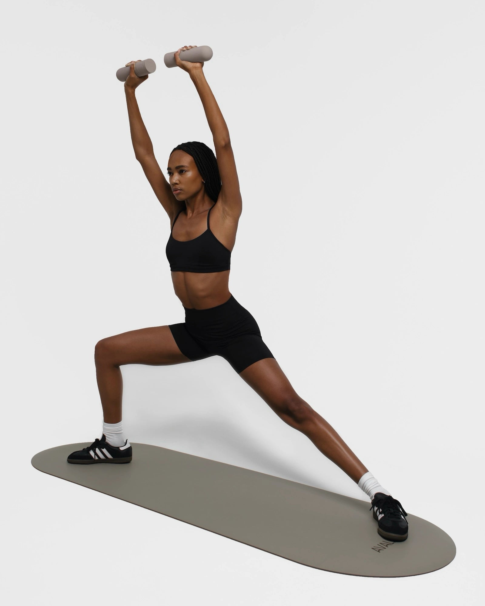 Gym girl in black sport wear doing glutes workout on a beige mat, lunge and holding beige silicone dumbbells