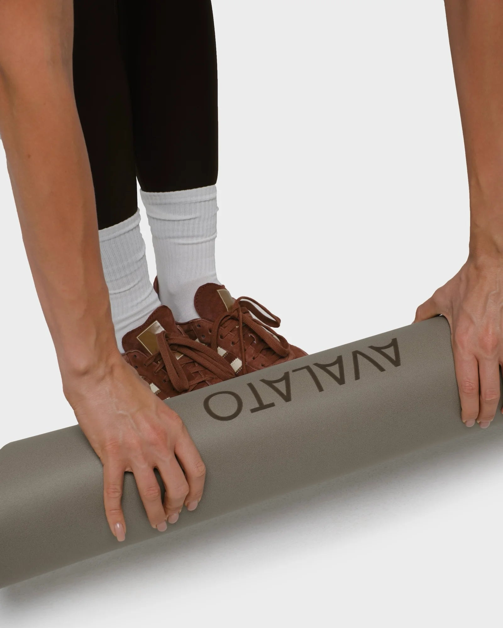 Close-up of hands rolling up a beige exercise mat, with legs in black gym leggings