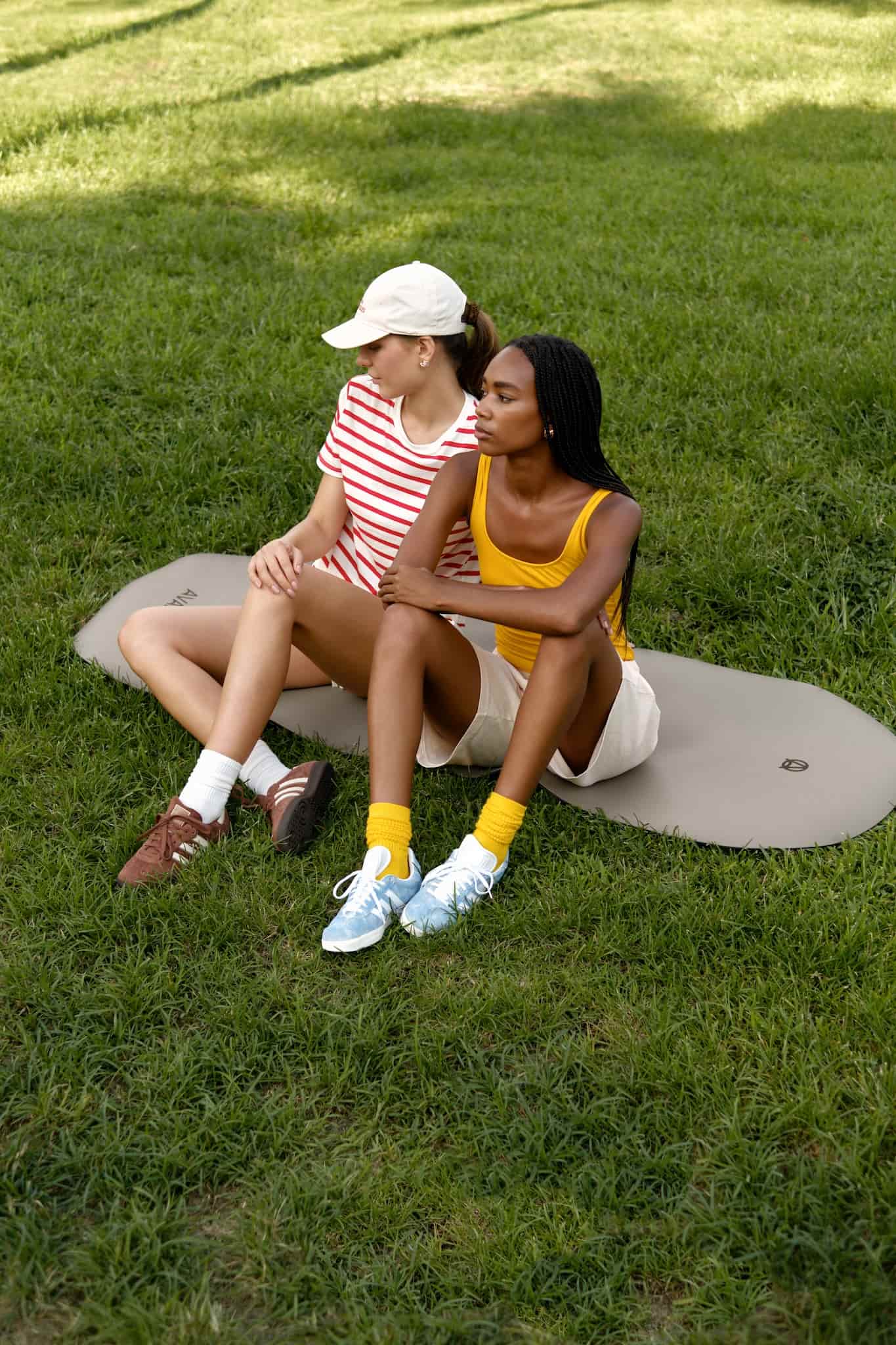 Two sporty women sitting on AVALATO exercise mat in a park.