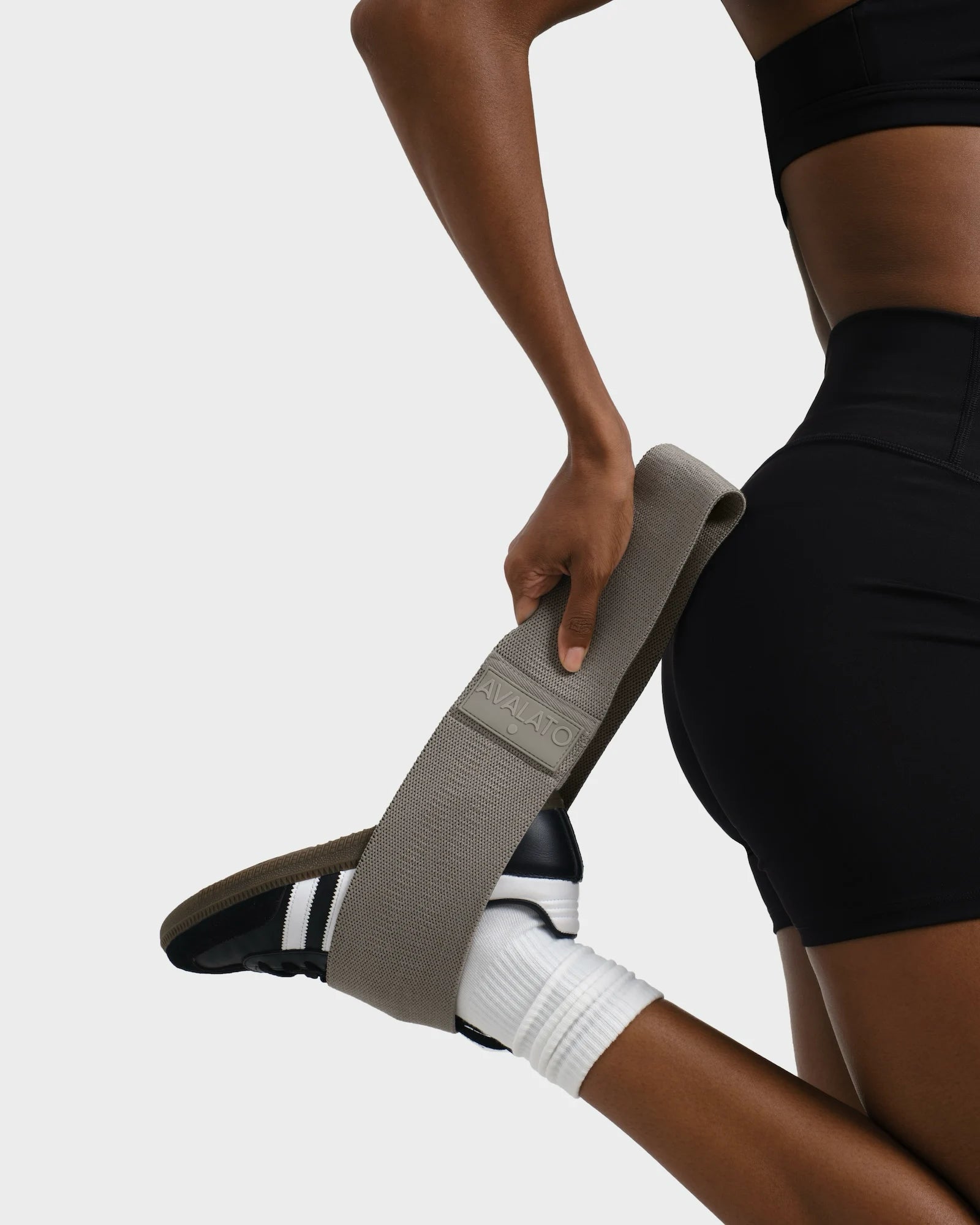 Woman in black workout outfit stretching her leg using a beige resistance band