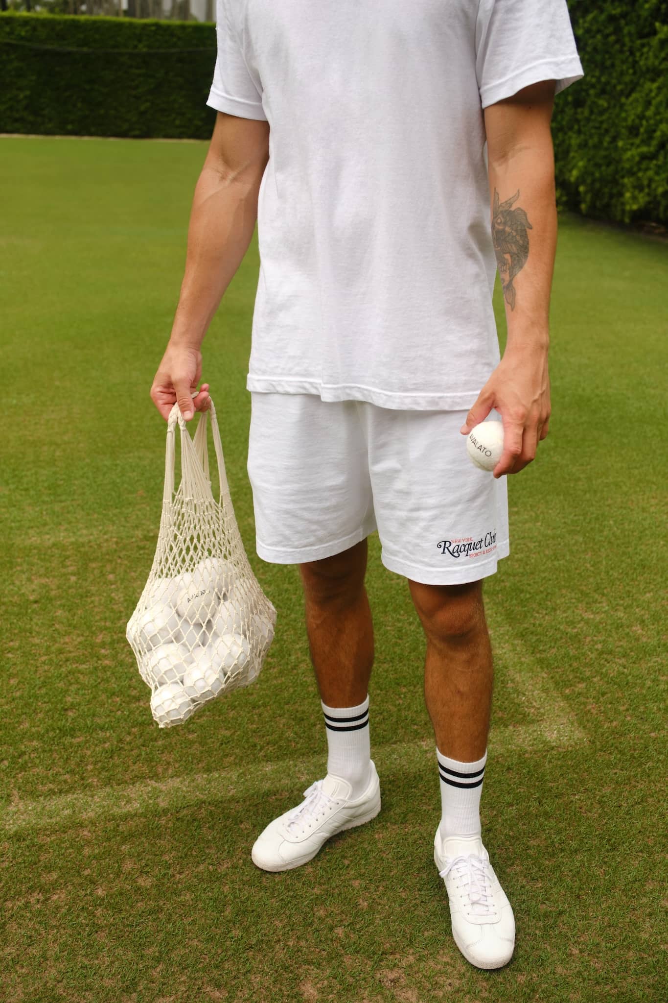 Male tennis player in vintage attire holding a net bag filled with white tennis balls on old schooled grass court