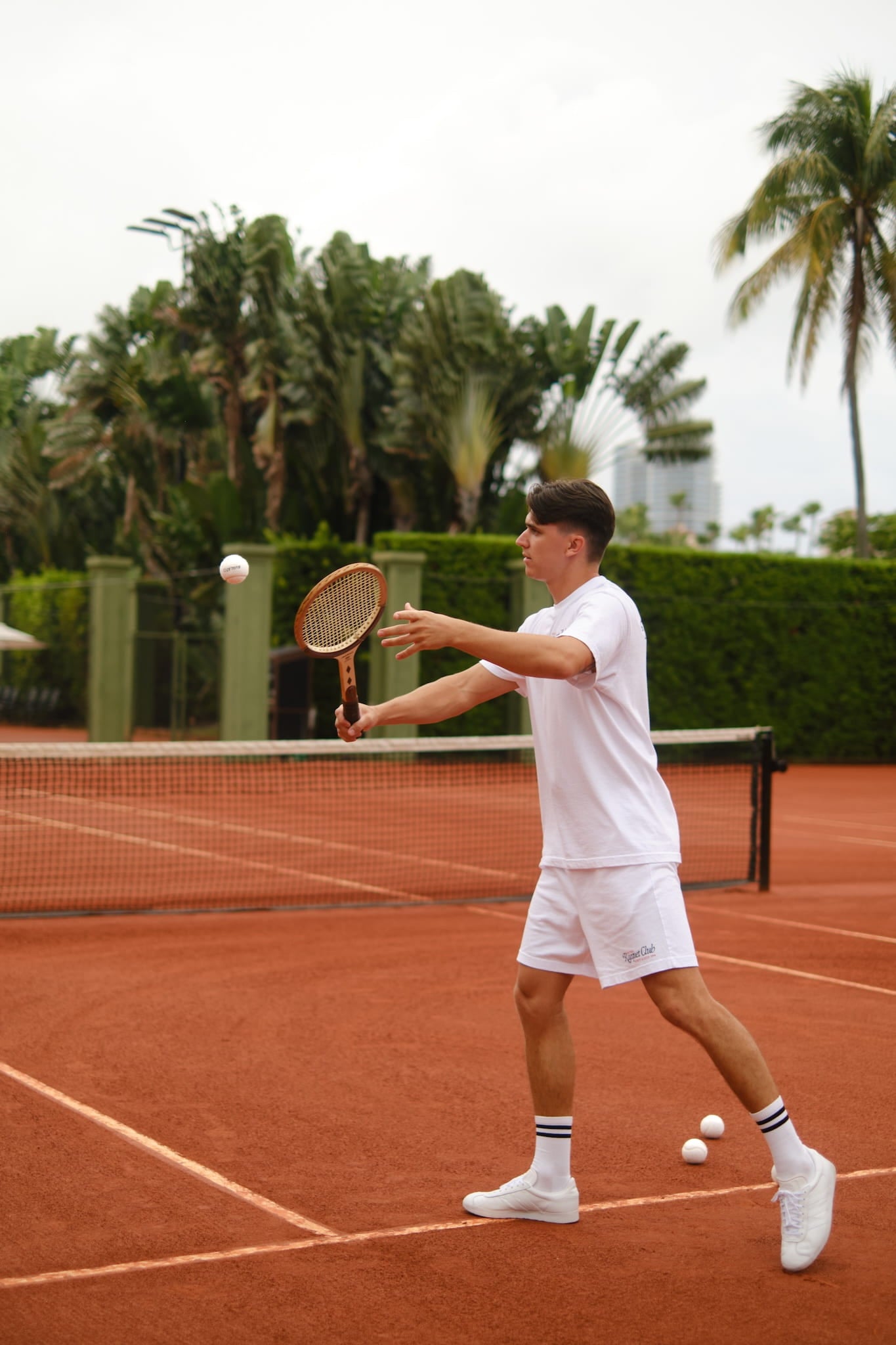 Male tennis player in vintage attire hitting a white tennis ball with a wooden racket