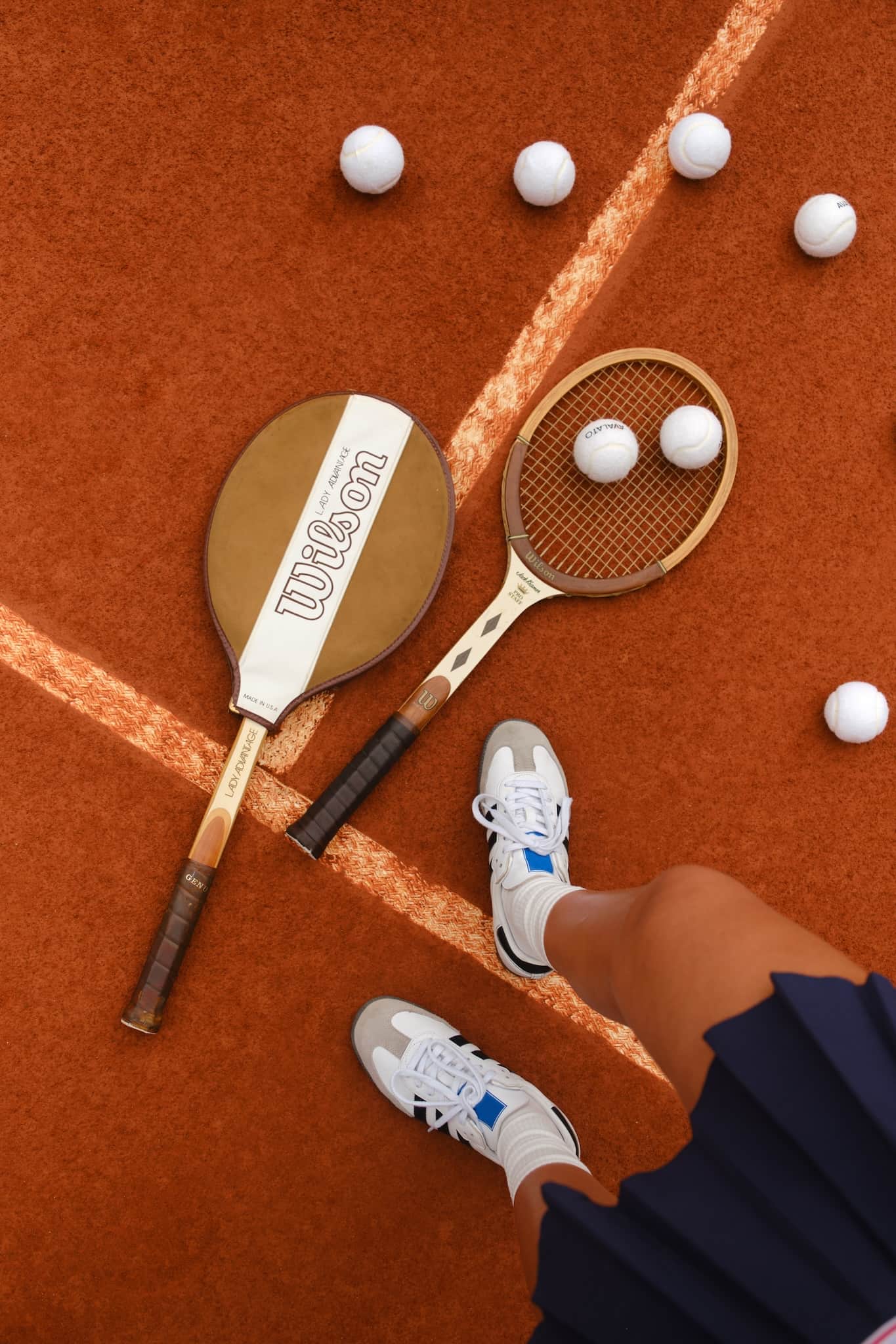 Top view of two wooden tennis rackets and vintage tennis balls on a clay court