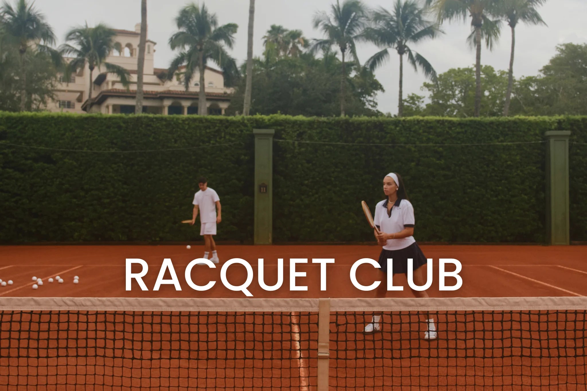 Two tennis players in vintage attire on a clay court with "Racquet Club" text overlay, surrounded by palm trees and a building in the background