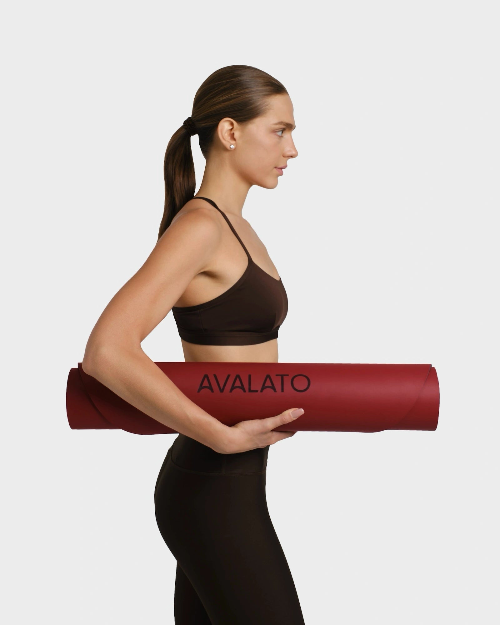 Side profile of a woman in black workout outfit carrying a red avalato exercise mat