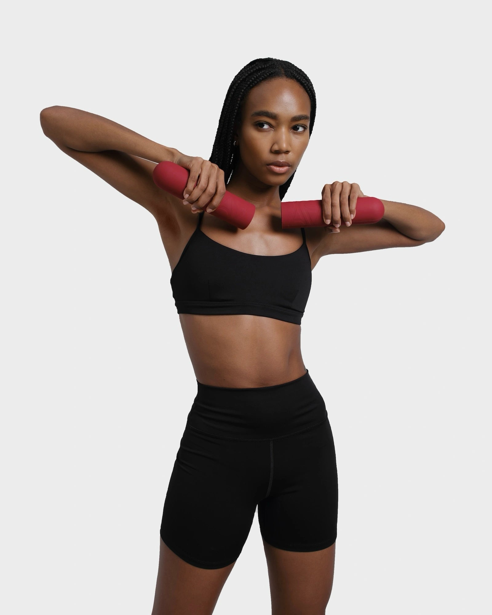 Gym girl in black outfit standing and exercising with red silicone dumbbells