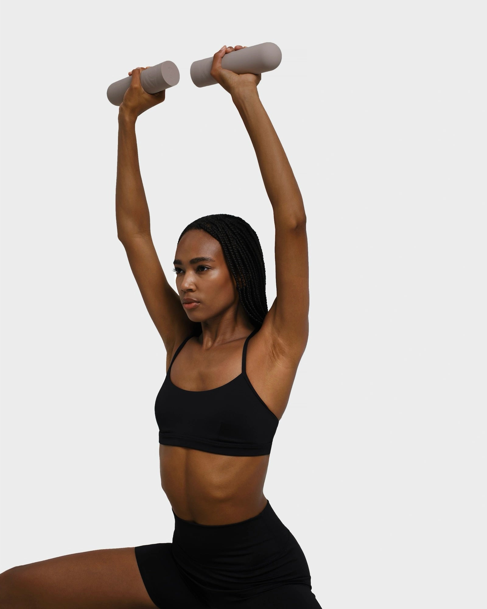 Woman in black workout outfit lunging with beige dumbbells held overhead