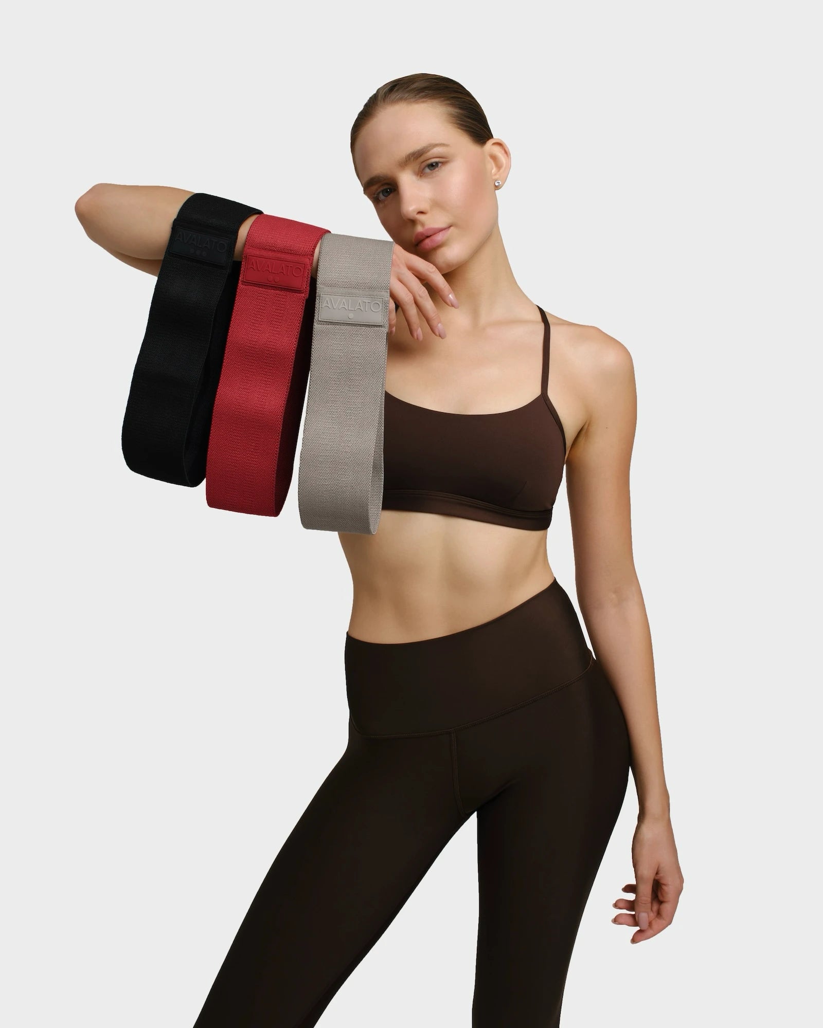 Woman in gym outfit holding black, red, and beige resistance bands