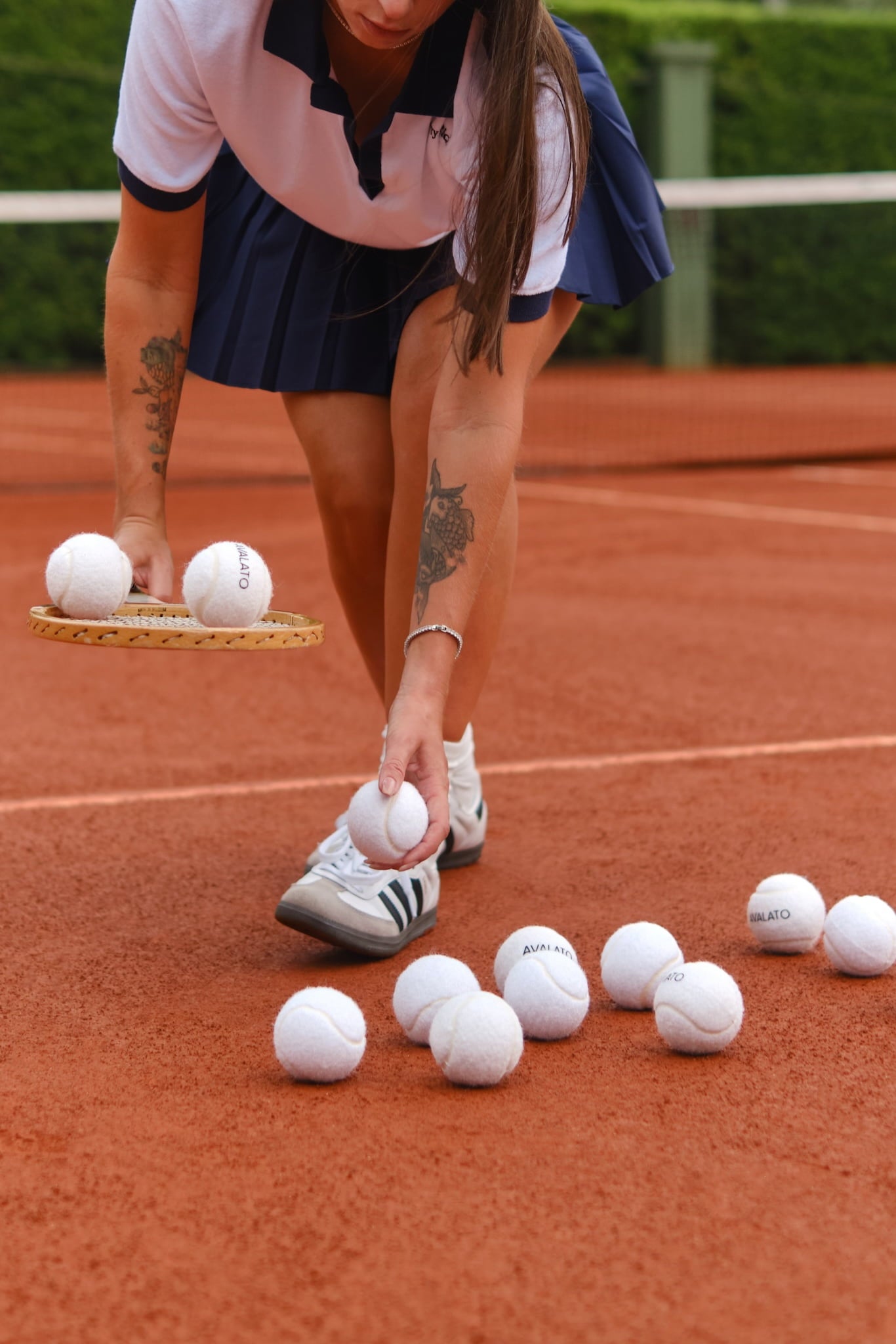 Female tennis player picking up white tennis balls with a wooden racket on a clay court