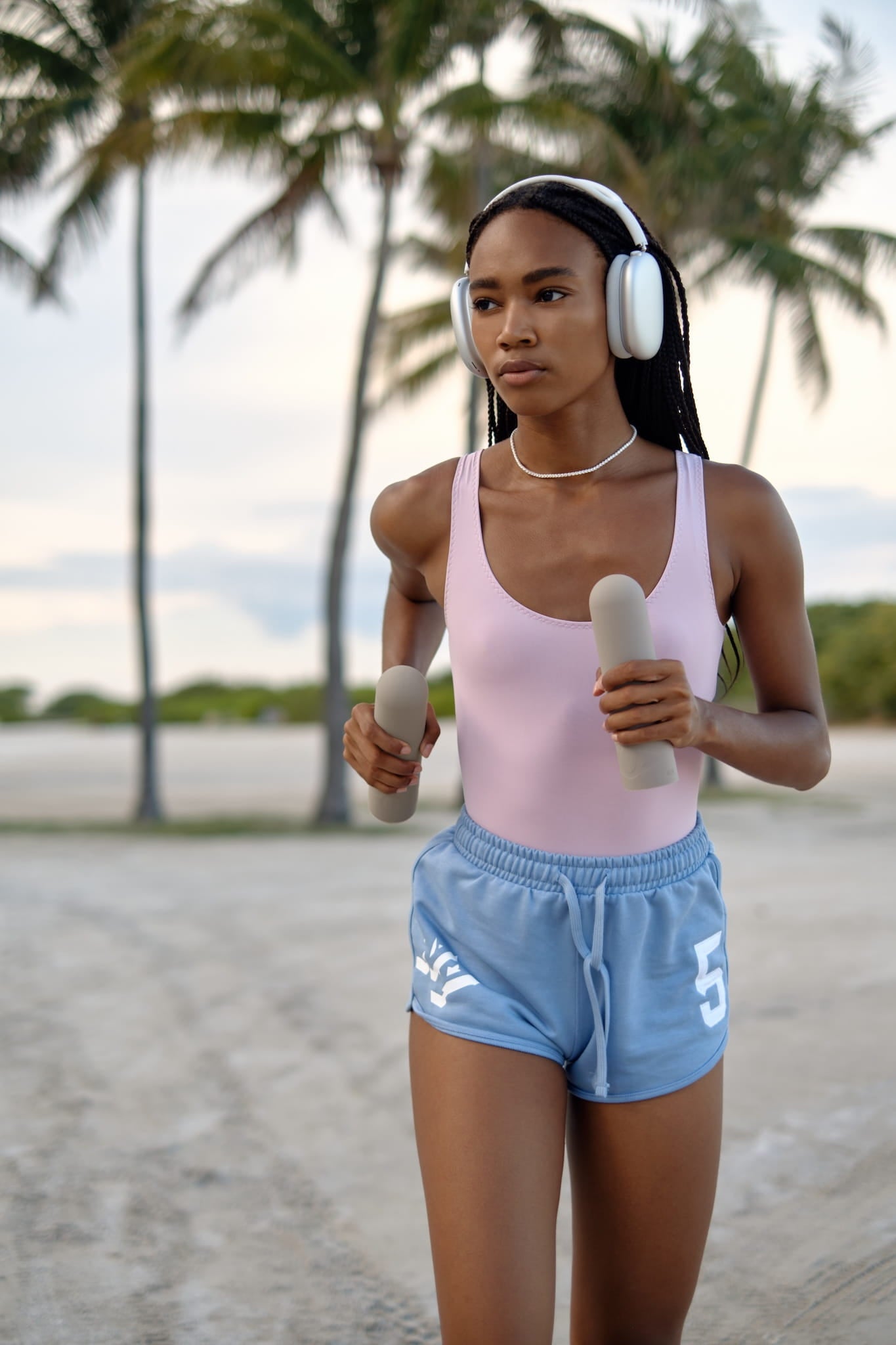 Athletic woman wearing activewear, running with AVALATO silicone dumbbells with palm trees in the background