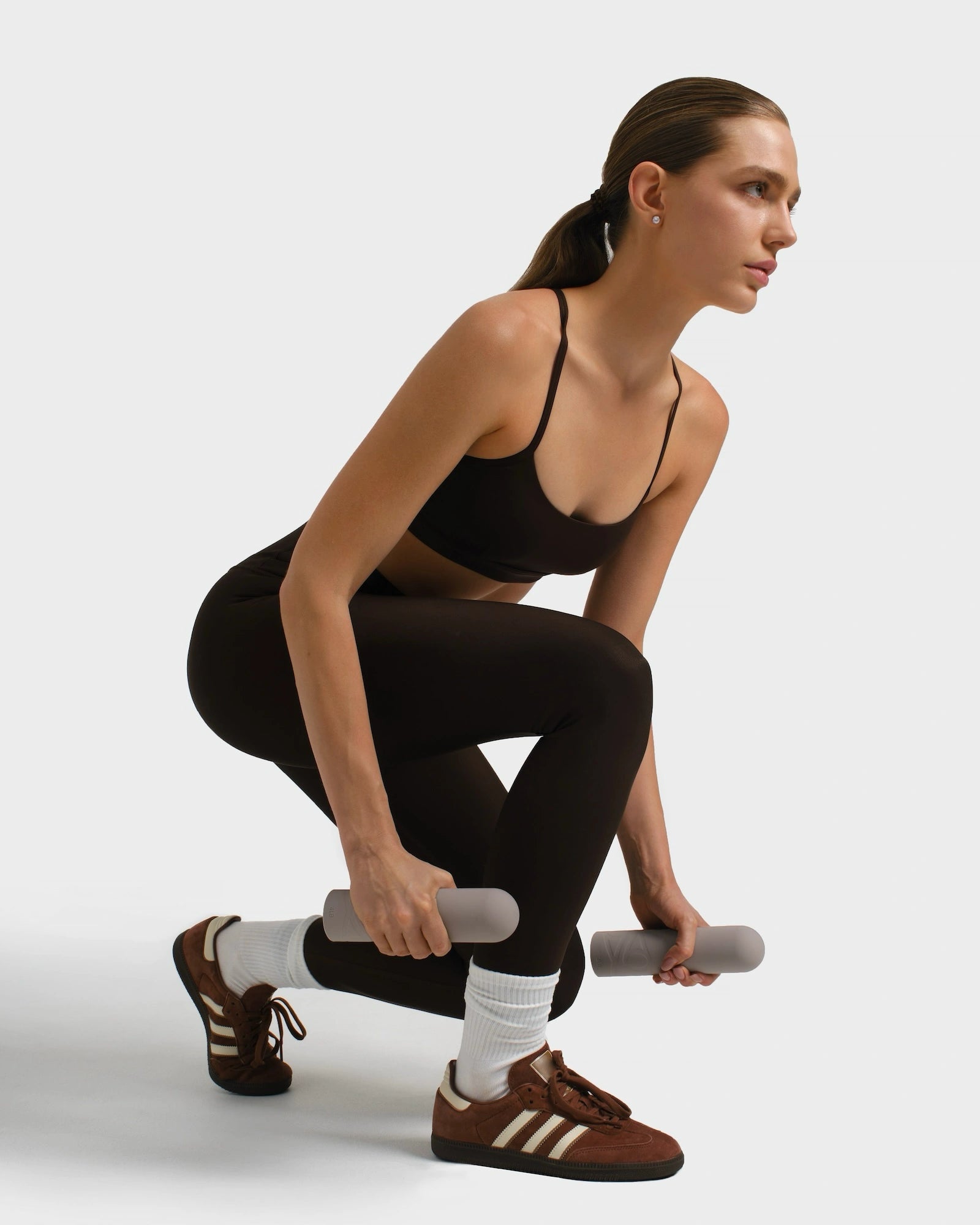 Woman in gym outfit doing her workout routine squatting while holding beige dumbbells