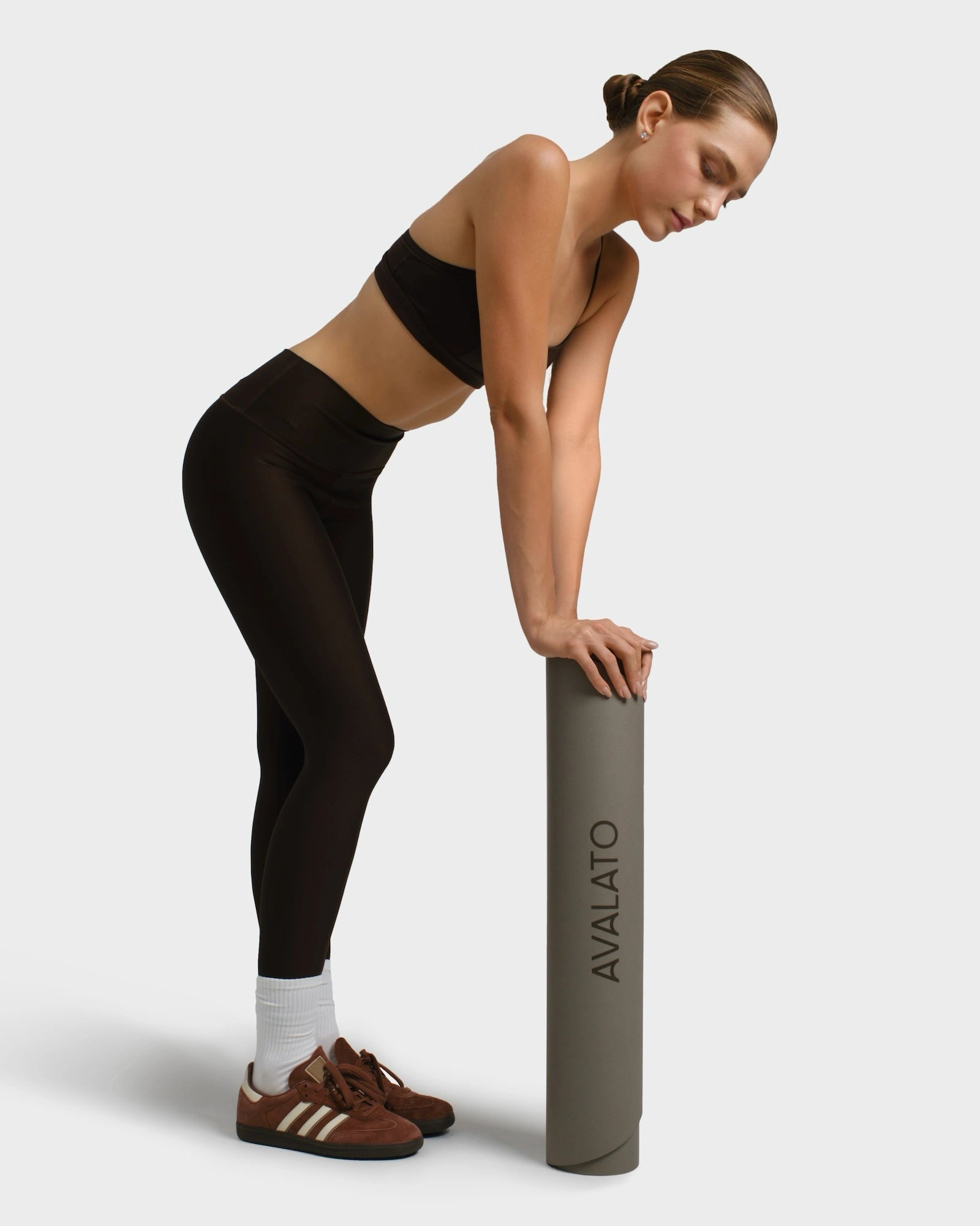 Woman in sport outfit standing and rolling up a beige avalato exercise mat