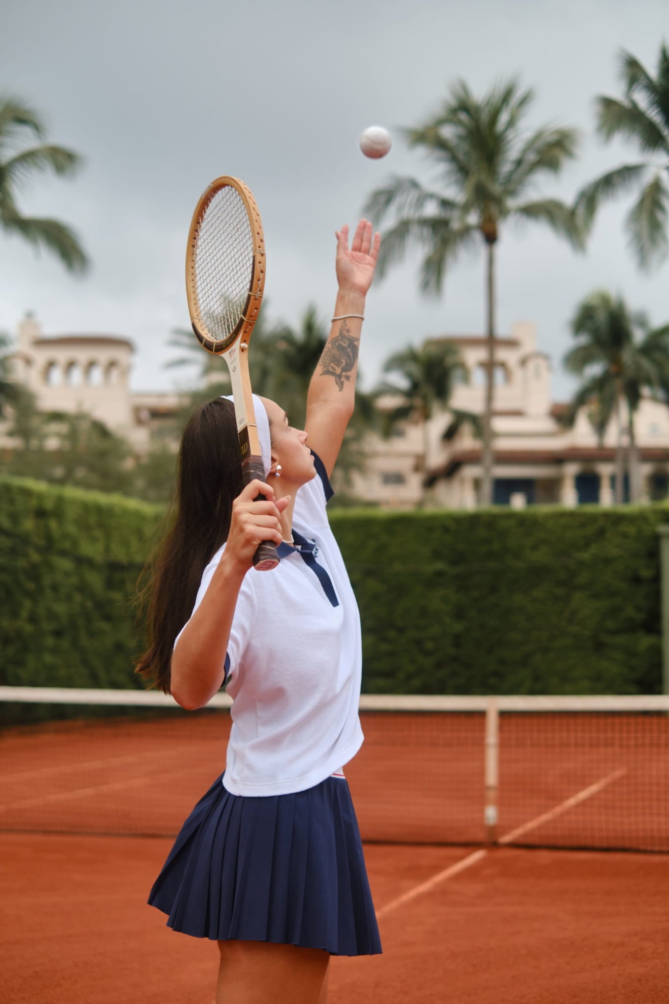 Female tennis player in vintage attire serving with a wooden racket