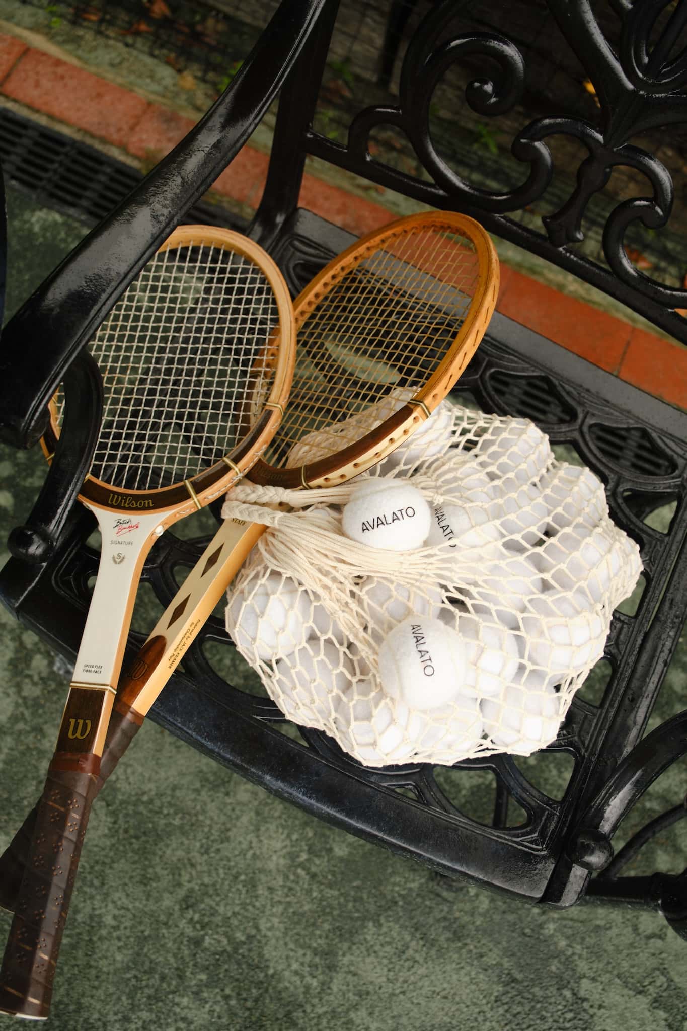 Two wooden tennis rackets and a net bag filled with vintage tennis balls on a black bench