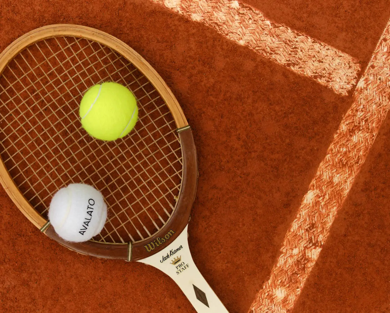 Vintage tennis racket on a clay court with one white and one yellow tennis balls